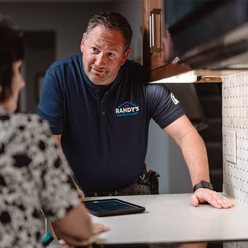 Randy consulting with a client in a kitchen, wearing Randy's Electric & Plumbing shirt.