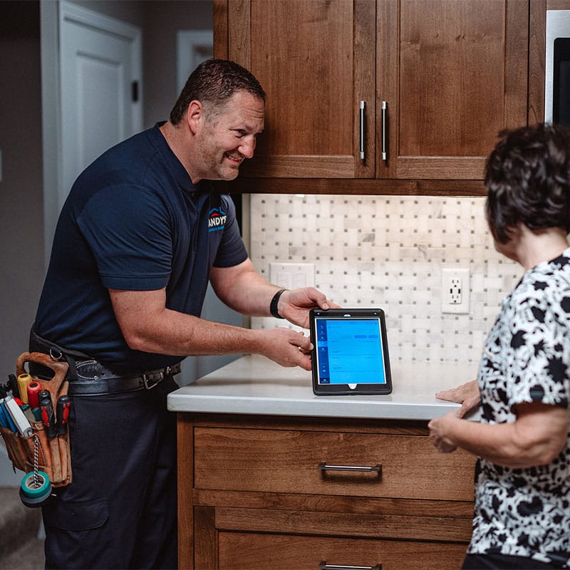 A handyman showing a woman a feature on a tablet in a kitchen setting.
