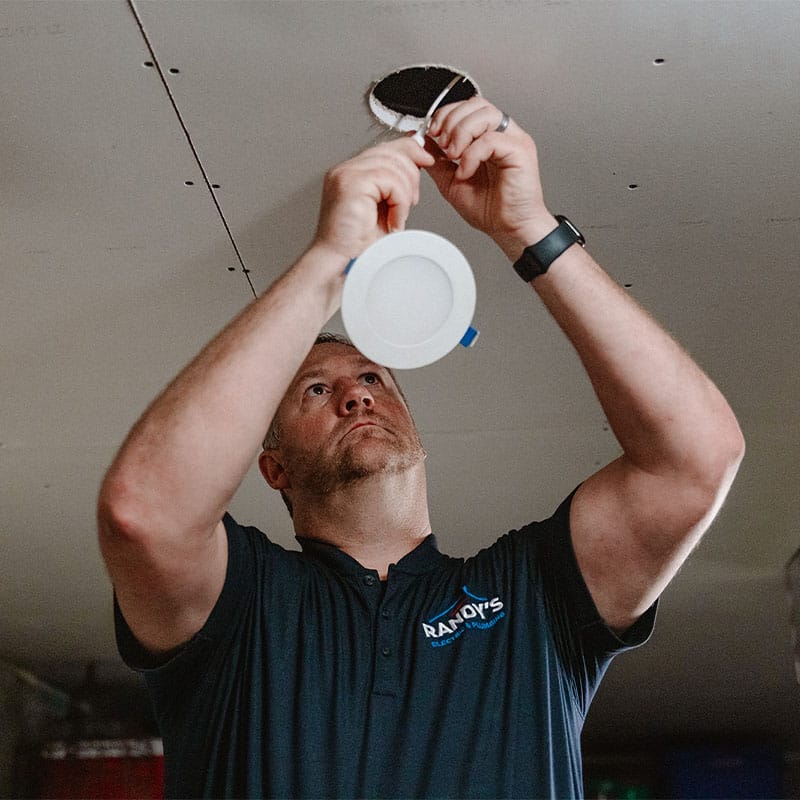 Worker installing ceiling light fixture in drywall.