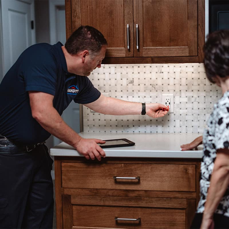 Electrician testing kitchen outlet with a voltage detector in a modern kitchen setting.