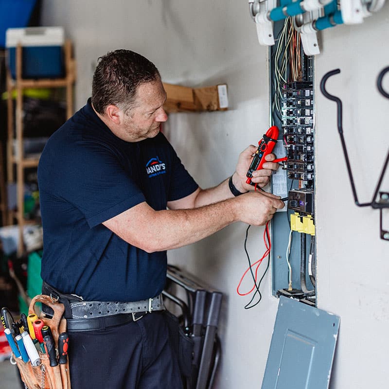 Electrician working on a circuit breaker panel with tools, wearing a blue Handy's shirt.