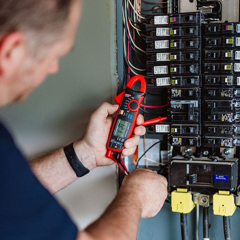 Person using a multimeter to check electrical panel, ensuring safety and functionality.