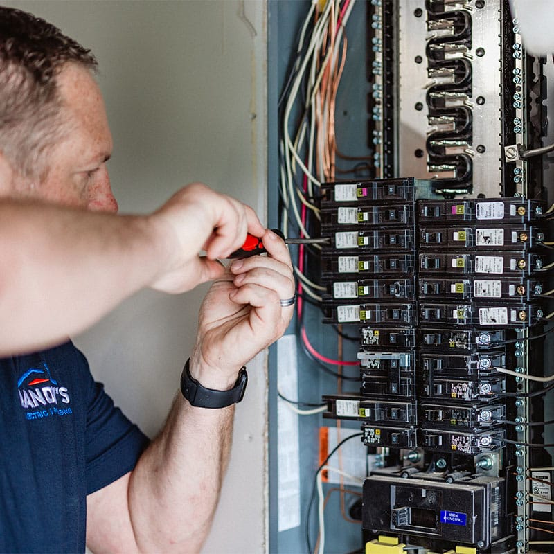 Electrician working on a circuit breaker panel with wires and tools.