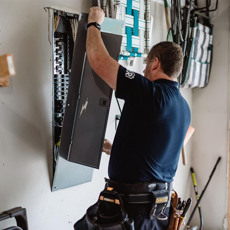 Electrician installing or repairing a panel box with tools in a garage.