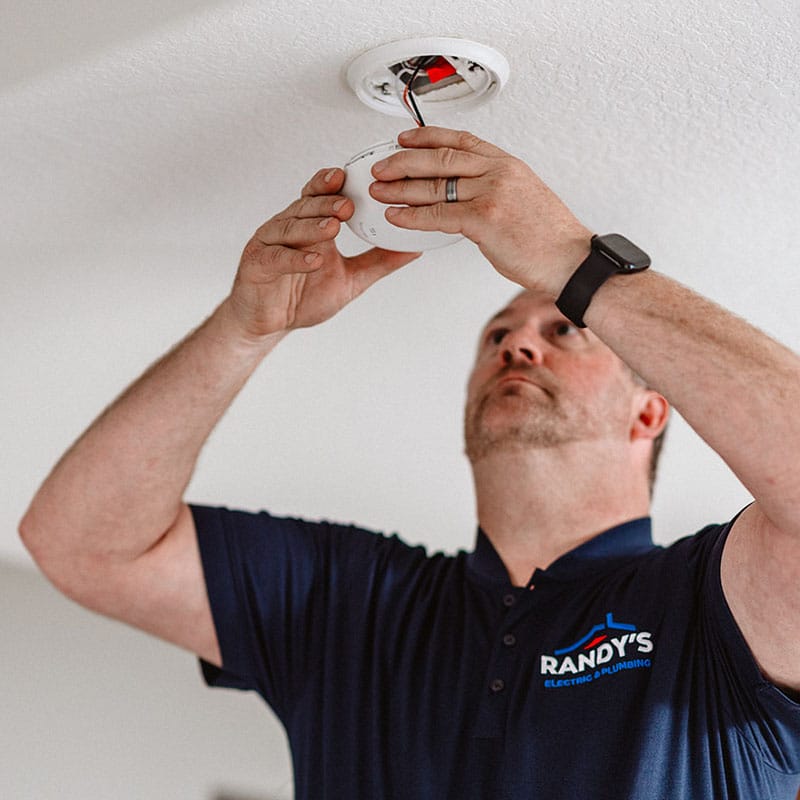 A person installing a smoke detector in a ceiling.