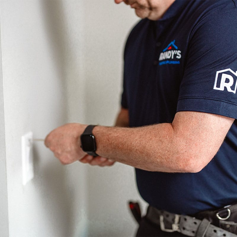 Person fixing wall outlet wearing Randy's Home Services shirt.