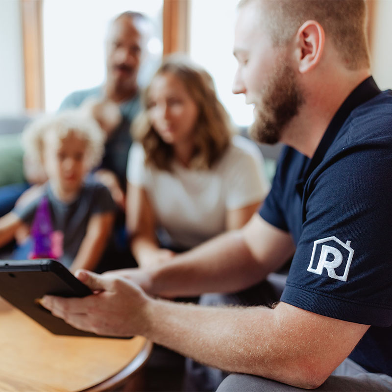 A man showing a tablet to a family in a living room setting.