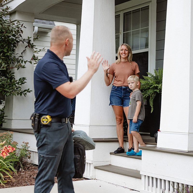 A man waving at a woman and child on a porch.