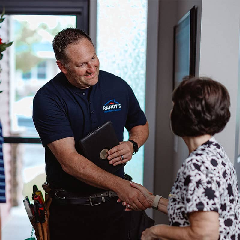 Handyman from Randy's Plumbing & Heating shaking hands with a customer indoors.