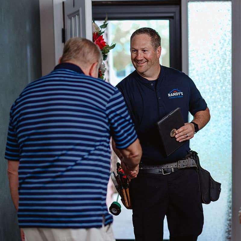 Man with tools and a customer shaking hands at the door.