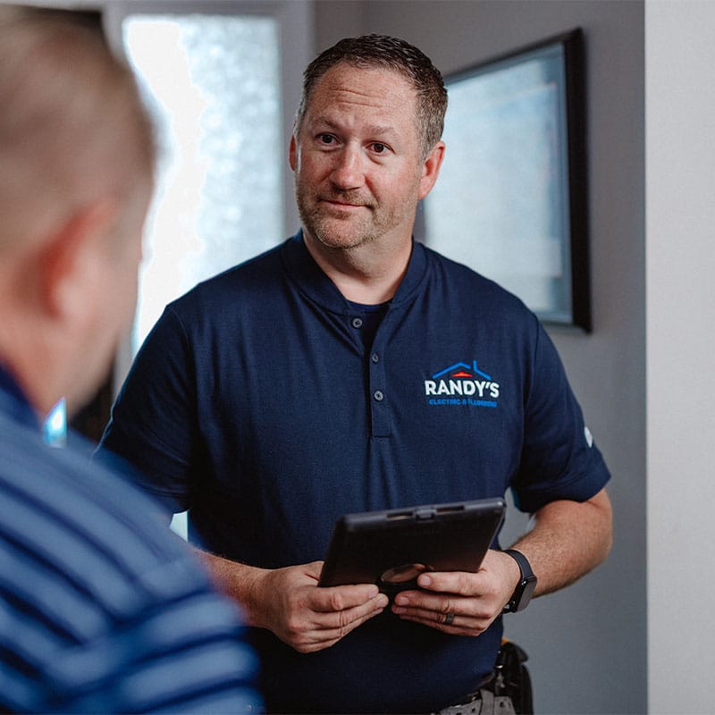 Man from Randy’s Electric & Plumbing holding a tablet, engaging in conversation indoors.