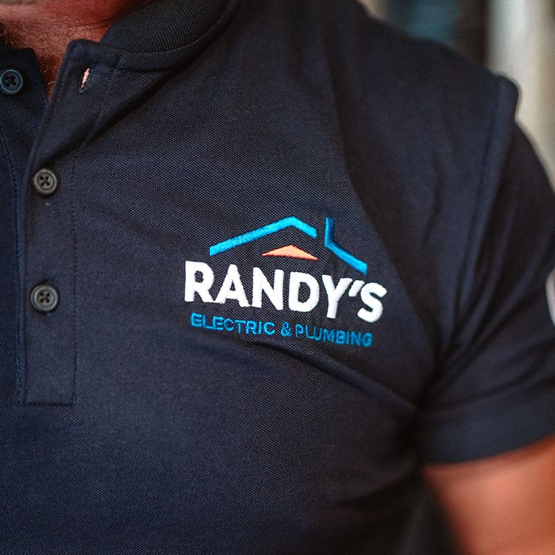Close-up of Randy's Electric & Plumbing logo on a dark polo shirt.