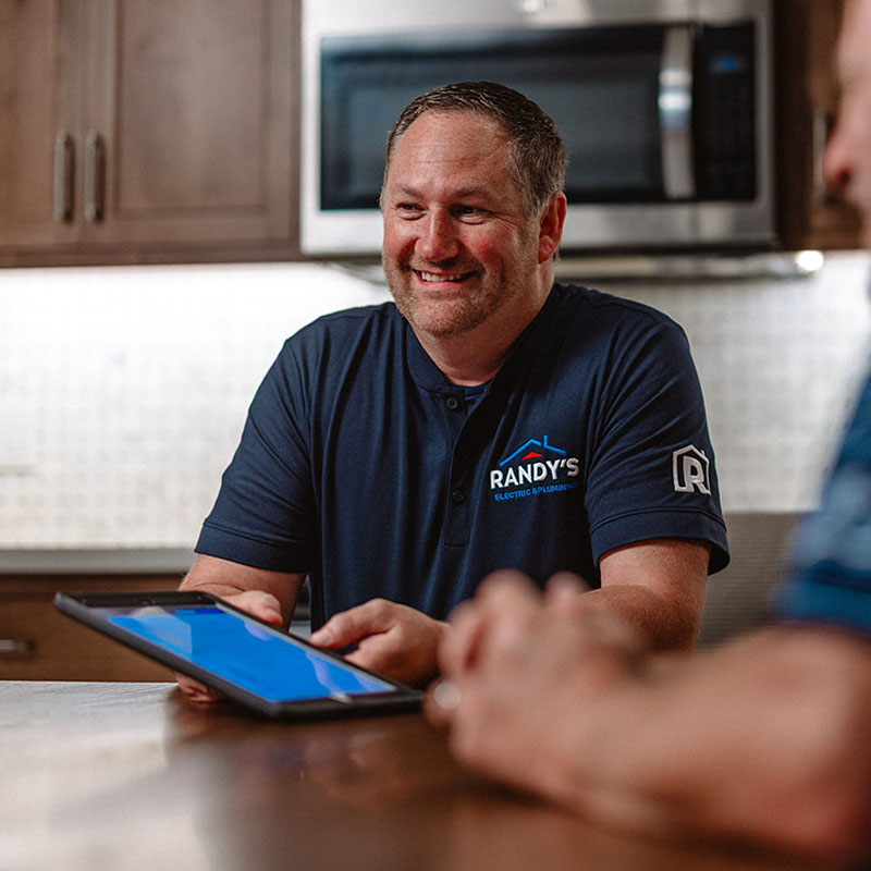 A man in a Randy's Electric & Plumbing shirt holding a tablet, smiling at a table.