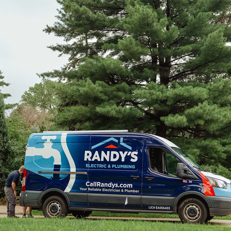 Randy's Electric & Plumbing van parked by trees, with logo and contact details visible.