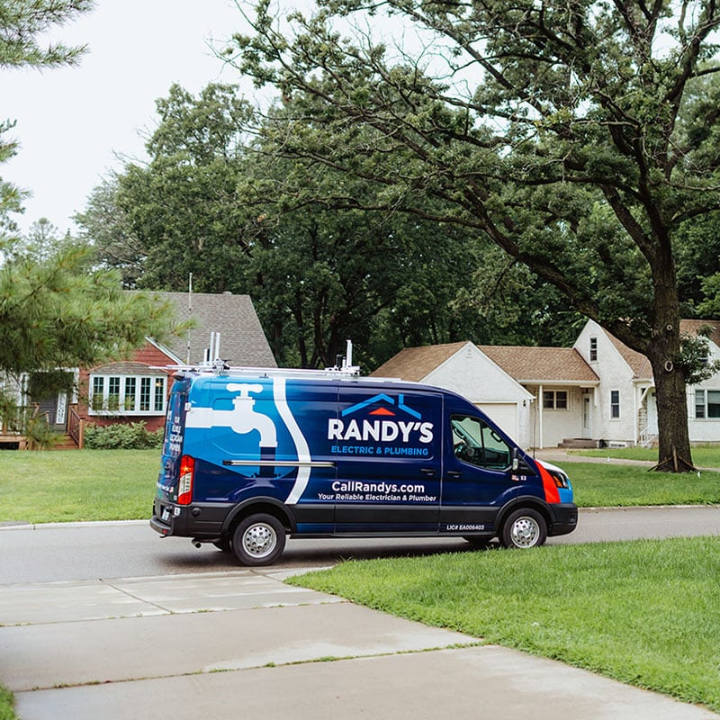 Randy's Electric & Plumbing service van parked in residential neighborhood with lush green trees.
