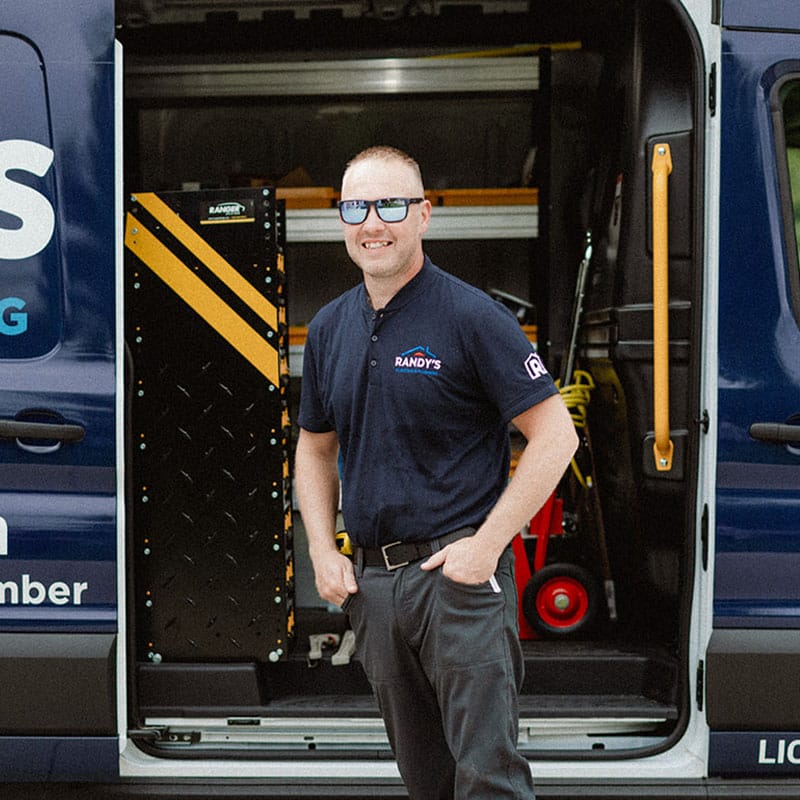 Randy standing by an open van, wearing a branded shirt and sunglasses, smiling confidently.