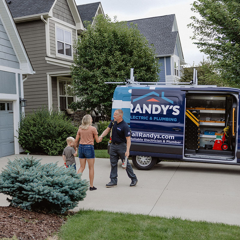 Electrician from Randy's Electric & Plumbing greeting a woman and child in front of a house.