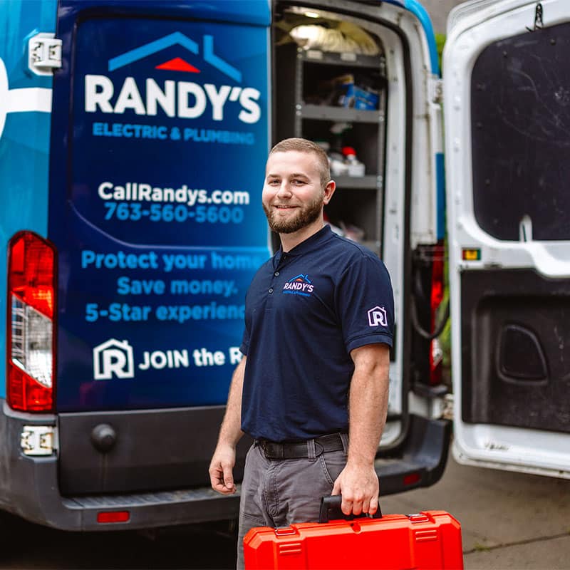 Man holding toolbox in front of Randy's Electric & Plumbing van, smiling.