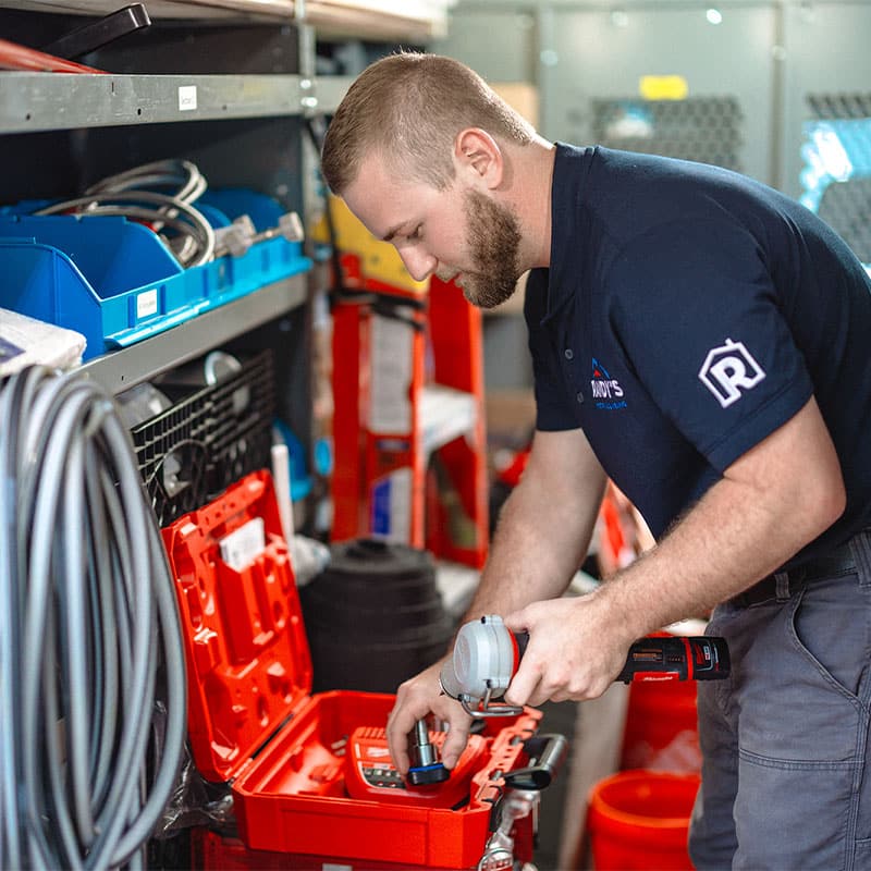 Worker in uniform organizing tools in a red toolbox inside a workshop or utility van.