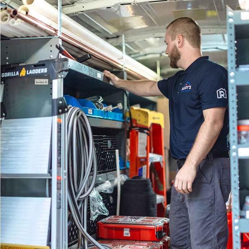 A man organizing tools in a utility van with shelves, ladders, and equipment.