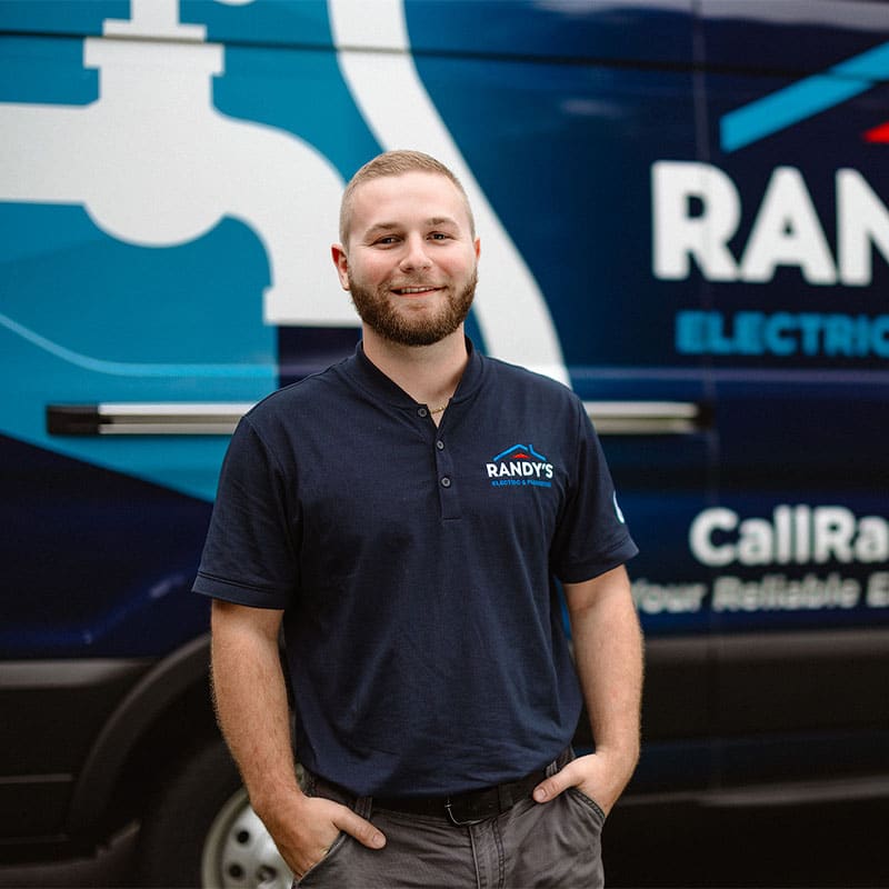A man in a Randy's Electric & Plumbing shirt stands in front of a company van.