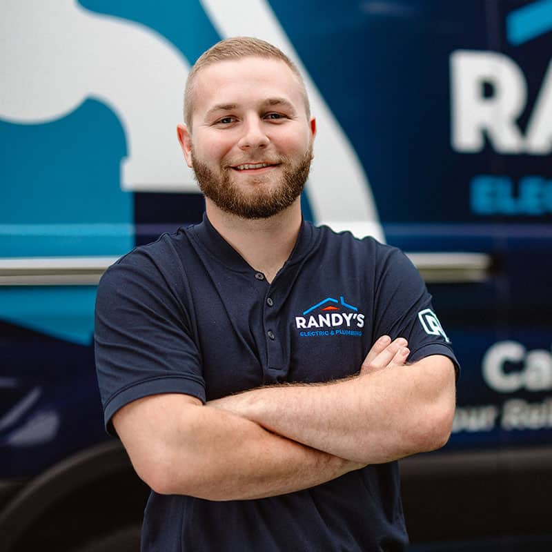Man in Randy's Electric & Plumbing shirt with arms crossed, standing in front of company van.