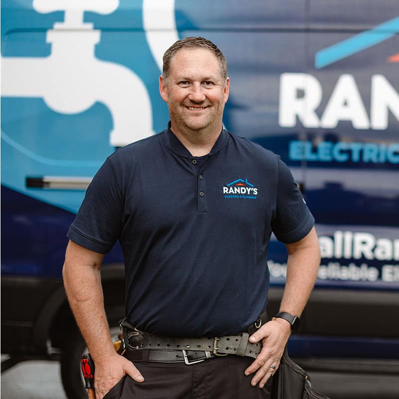Randy in front of company van, wearing a branded Randy's Electric & Plumbing shirt.