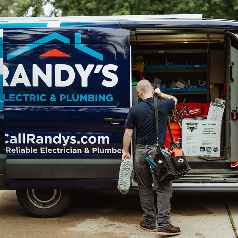 Electrician carries tools to van branded Randy's Electric & Plumbing, ready for service.