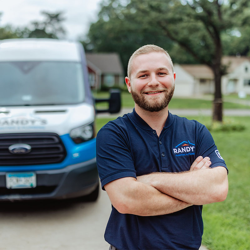 A man in a Randy's Electric shirt stands smiling in front of a branded service van on a residential street.