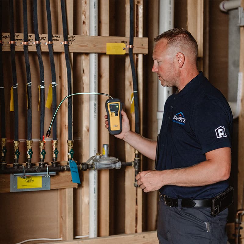 Person using a leak detector near pipes in a service area.