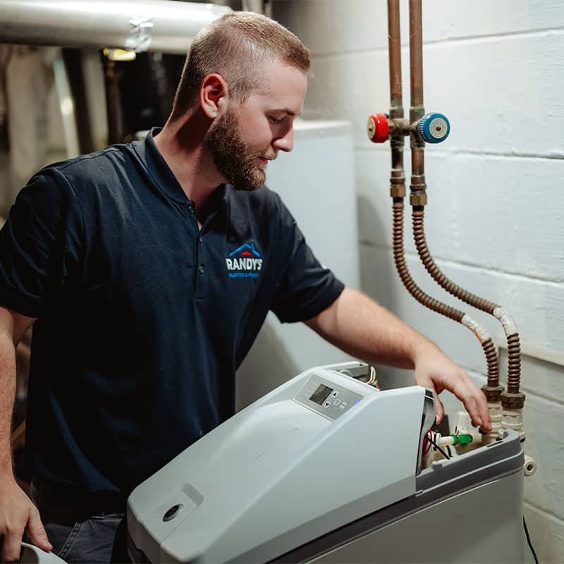 Man in Randy's Heating shirt repairing a boiler in a utility room.