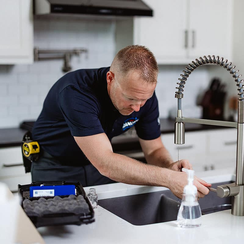 Plumber fixing kitchen faucet, using tools near sink in a modern kitchen setup.