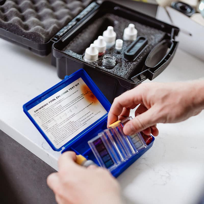 Person using a swimming pool chlorine test kit on a white surface.