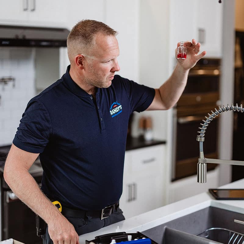 A man in a Randy's polo shirt inspects a vial of red liquid in a modern kitchen.