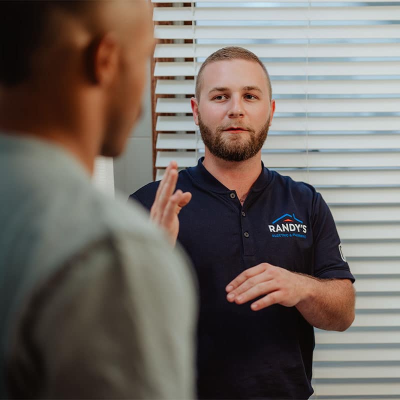 Man in Randy's uniform discussing with another person indoors near window blinds.