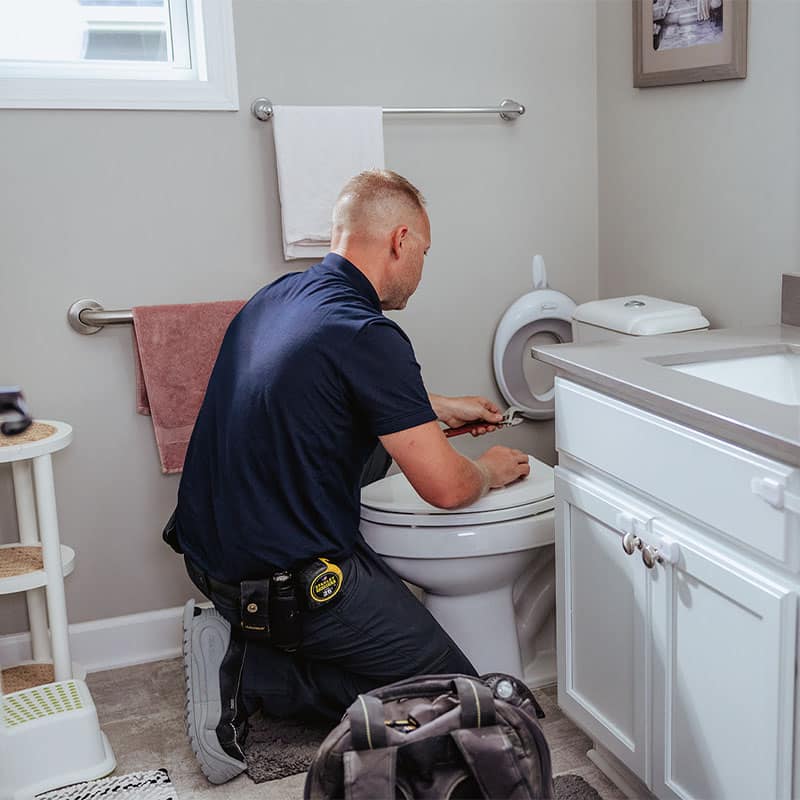 A plumber fixing a toilet in a bathroom, with tools and a tool bag on the floor.