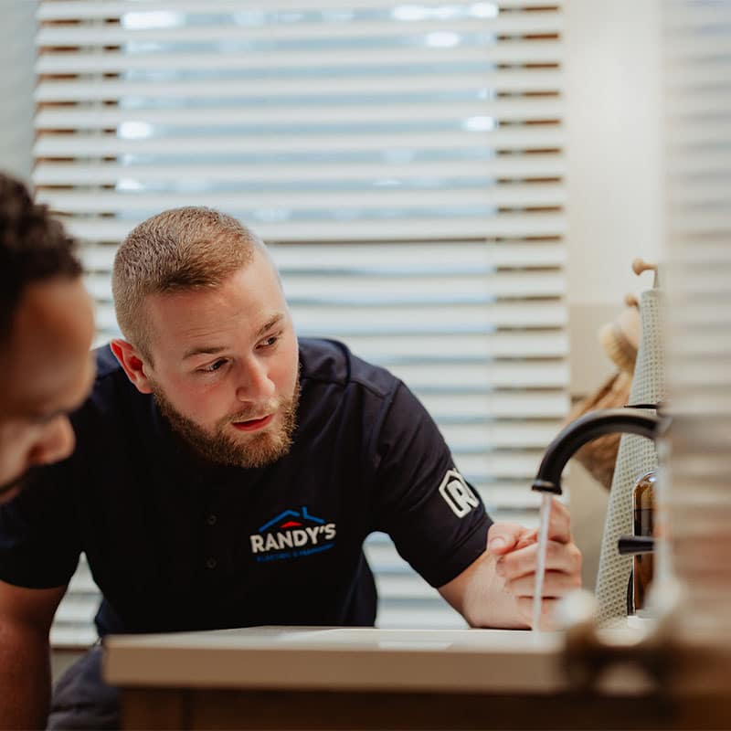 A Randy's employee inspecting a sink faucet in a brightly lit room.