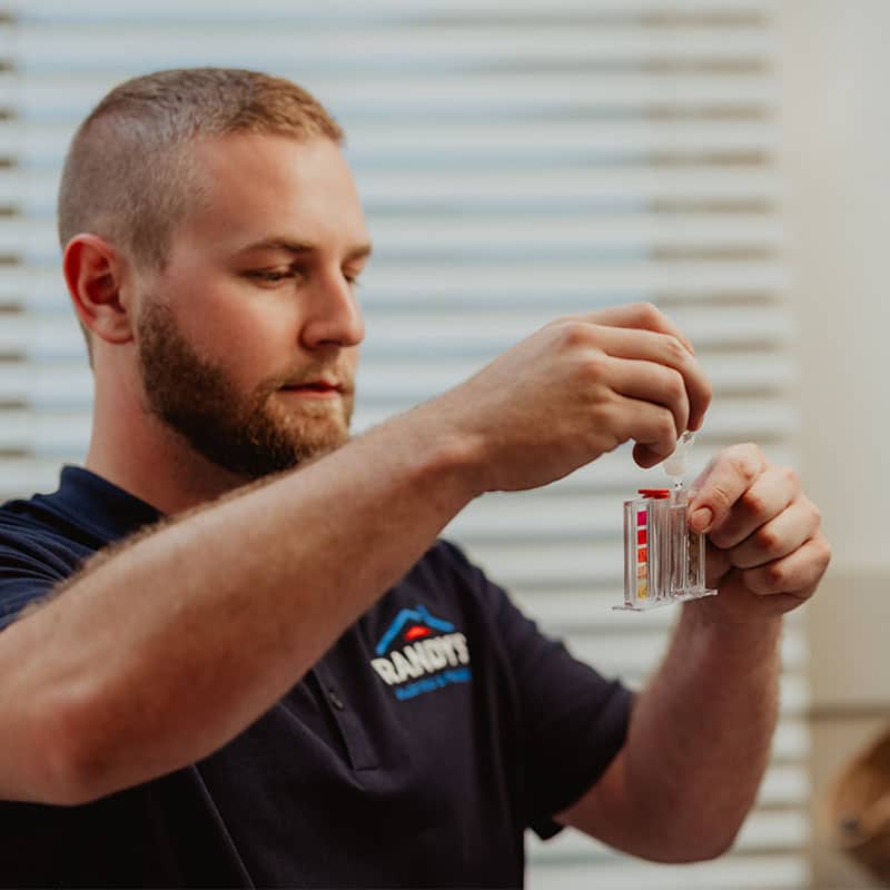 A man conducting a test with a dropper in a plastic container in front of blinds.