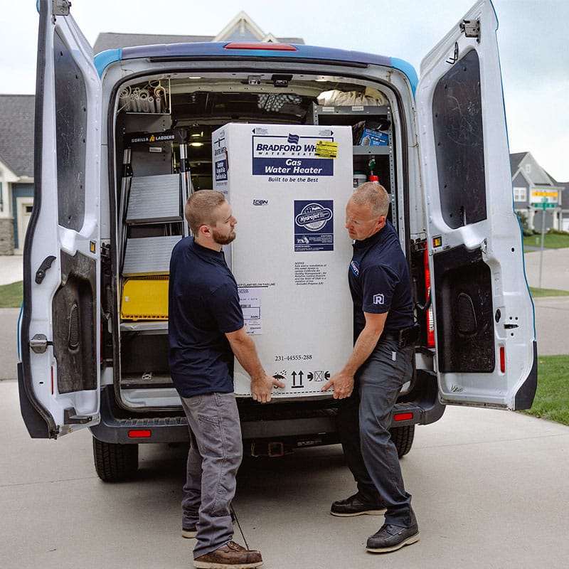 Two men loading a Bradford White gas water heater into a service van.