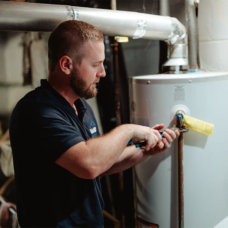 Man repairing a water heater with tools in a basement setting.