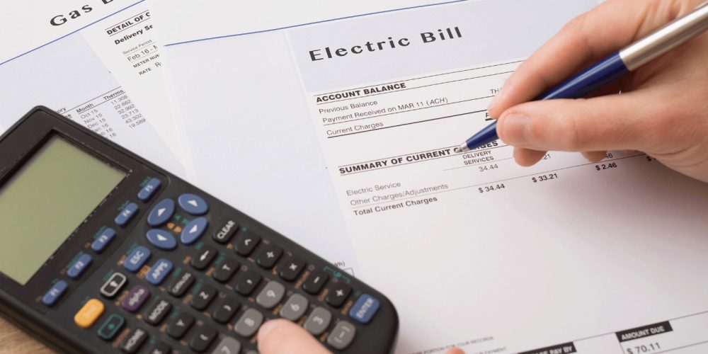 Hands with pen and calculator reviewing electric and gas bills on a wooden desk.