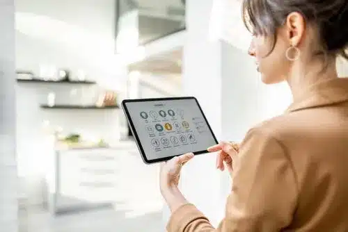 A woman using a tablet to control a smart home system in a modern kitchen.