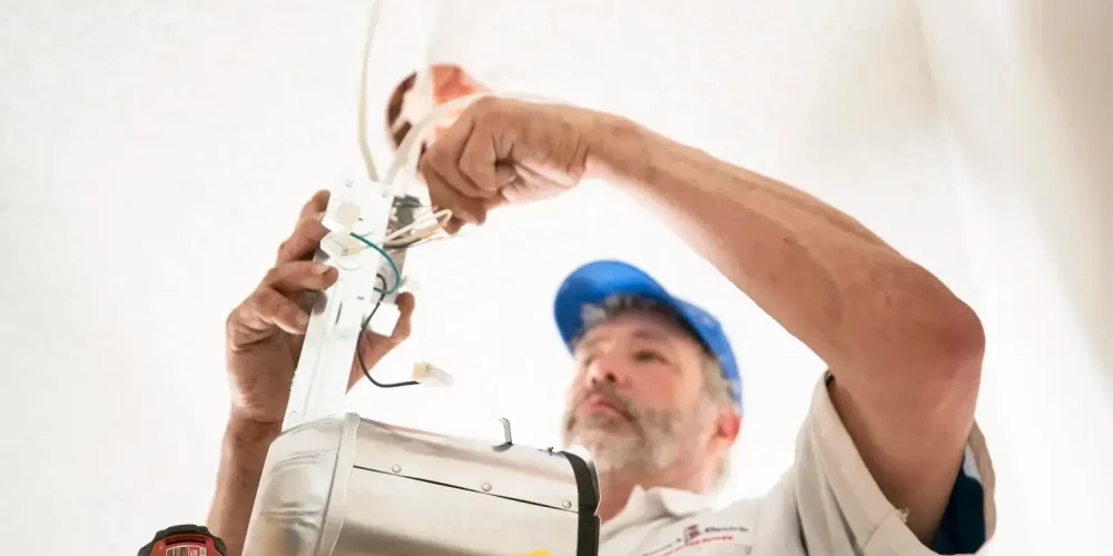 Electrician installing ceiling light fixture, close-up view from below.