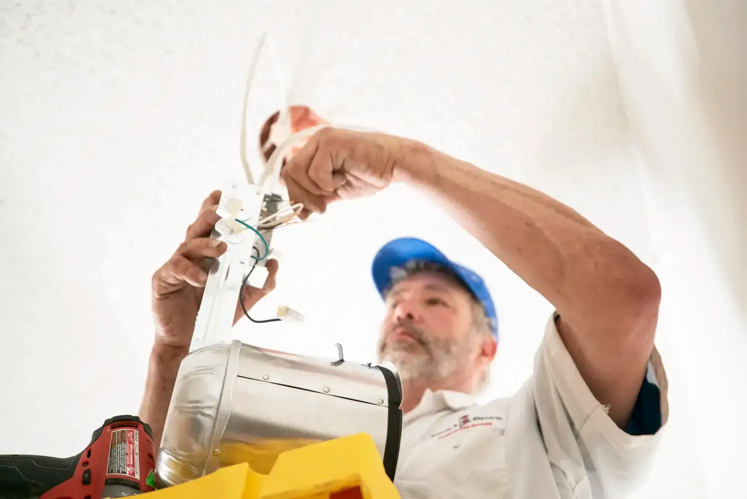 Electrician installing ceiling light fixture, close-up view from below.
