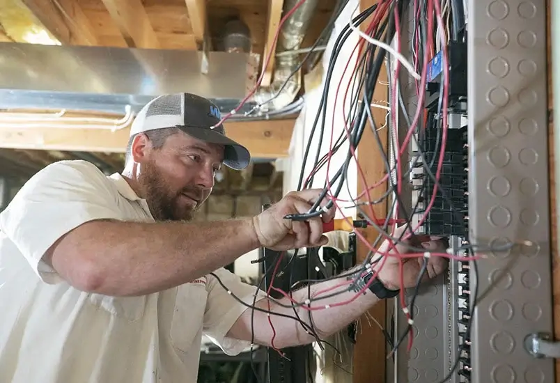 Electrician working on a circuit breaker panel in a basement.