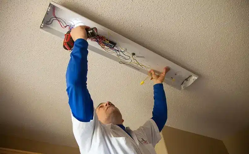 Electrician fixing ceiling light wiring with a drill.
