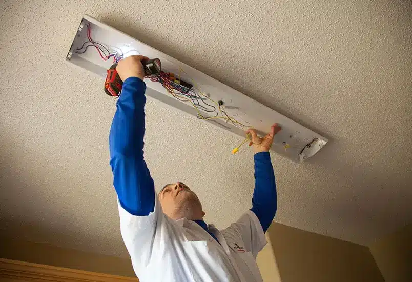 Electrician fixing ceiling light wiring with a drill.