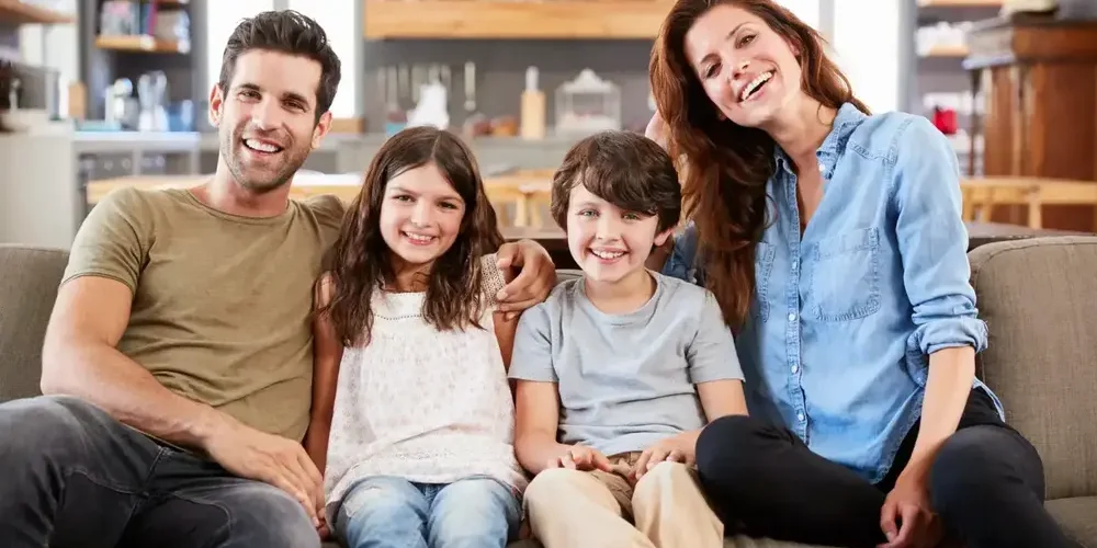 Happy family of four sitting on a couch at home, smiling together.