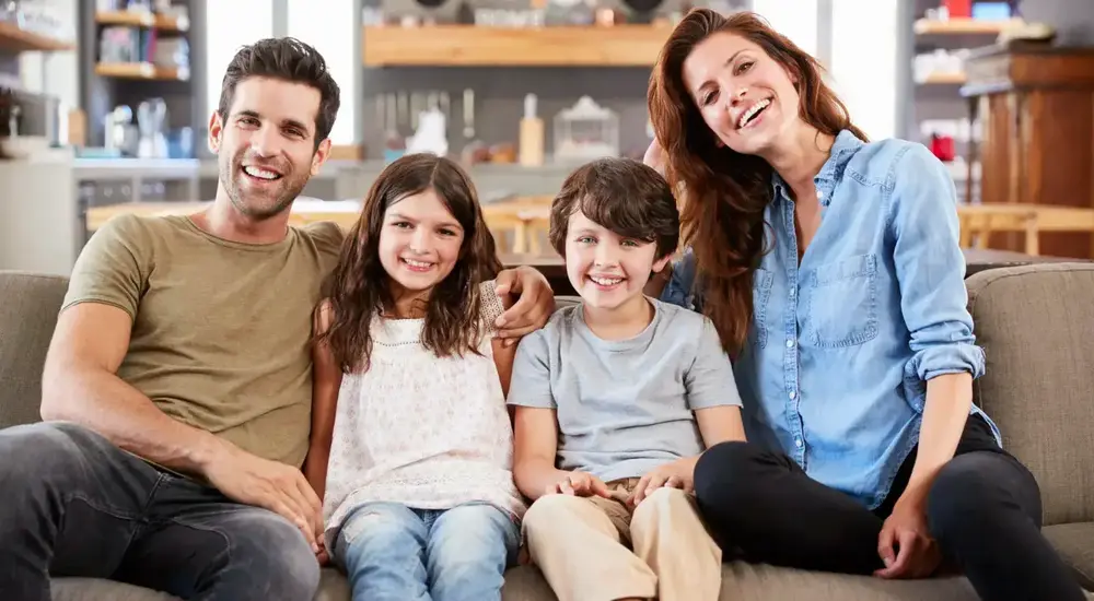Happy family of four sitting on a couch at home, smiling together.