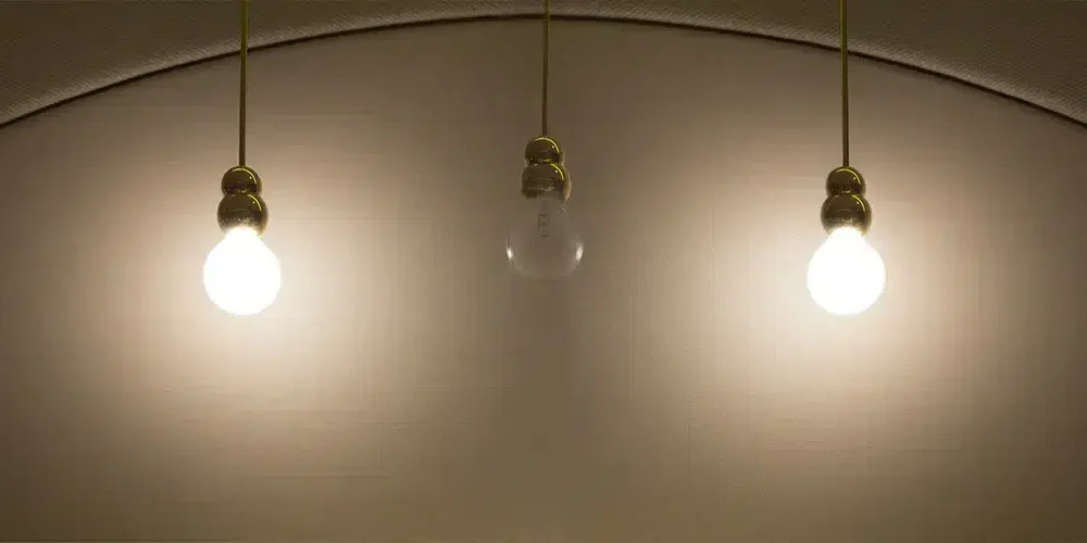 Three hanging light bulbs lit against an arched ceiling, with the center bulb unlit.